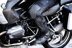 Black heated pants by Gerbing, worn by a rider on a motorcycle, with padded knees and ribbed details.