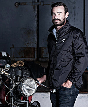 Black heated jacket liner by Gerbing, with a white chest logo, worn by a man next to a motorcycle.