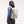 Light taupe Flap Pack Bag by Got Bag, worn on a woman's back, with a water bottle in the side pocket and colorful zipper pull.