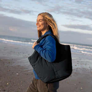 Dark blue padded tote bag by Got Bag carried by a woman in a blue hoodie on a sunny beach.