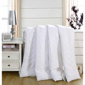 White silk comforter by HealthyLine, quilted with scalloped stitching, folded over a bed in a bright bedroom.