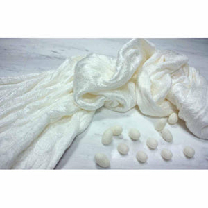 White silk comforter by HealthyLine, draped on a light surface with raw silk cocoons.