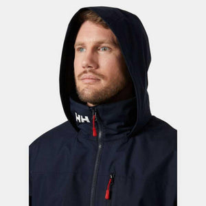 Navy blue hooded men's midlayer jacket by Helly Hansen, shown on a man with hood up, featuring white HH logo and red zipper pulls.