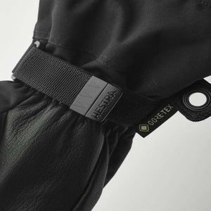 Black leather and fabric 5-finger gloves by Hestra with an adjustable strap, HESTRA buckle, GORE-TEX tag, and metal grommet.