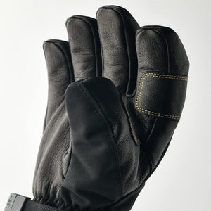 Black leather 5-finger glove by Hestra, with gold contrast stitching, black fabric sections, and a buckle showing 'HESTA', in a close-up view.