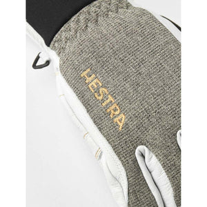 Short glove with grey textured fabric and white leather accents by Hestra, featuring a gold embroidered logo and black knitted cuff.