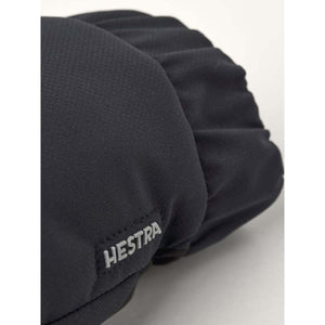 Dark grey/black textured gloves by Hestra, featuring a silver Hestra logo on the cuff, in a close-up view.