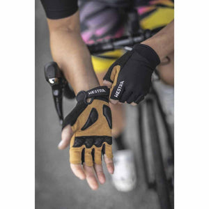 Black and tan Bike Guard Short 5-Finger Gloves by Hestra, with padded palms, worn by a cyclist gripping handlebars.