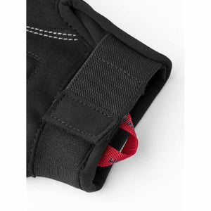 Black 5-finger gloves by Hestra, close-up of wrist with velcro strap, white stitching, and red pull tab.
