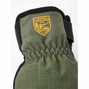 Green ripstop gloves by Hestra, featuring a yellow embroidered logo shield, elasticized wrist, and black adjustable strap.