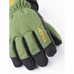 Green and black technical gloves by Hestra, featuring a textured green fabric, black reinforced fingers, and a yellow HESTRA logo.