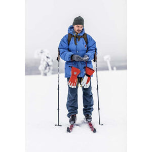 Grey thin inner gloves by Hestra, worn by a man holding a phone, with red and white outer gloves hanging from his blue jacket in snow.