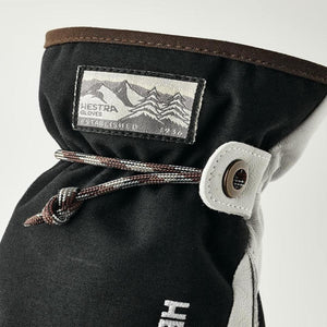Black and grey mitten by Hestra with a mountain logo label, patterned drawstring, and leather eyelet.