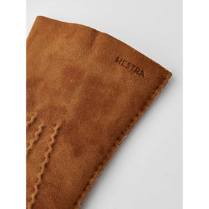 Brown suede leather glove by Hestra with subtle embossed logo and visible stitching detail on the fingers.