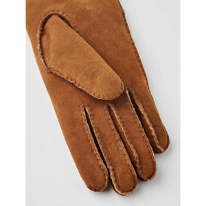 Brown suede leather women's gloves by Hestra, featuring hand-sewn detailing, a prominent thumb overlay, and visible finger seams, cropped.