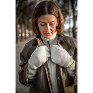 Fuzzy light grey mittens by Hestra, worn by a woman in a brown jacket looking down.