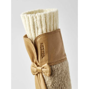 Tan leather mitten by Hestra, with a cream ribbed knit cuff, a small leather bow, and fuzzy lining.
