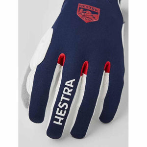 Navy blue and white ski gloves by Hestra featuring red finger accents, 'Hestra' text, and a red brand logo patch.