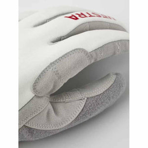 White and grey ski glove by Hestra, with a red HESTRA logo and textured suede-like patches on fingers and palm.