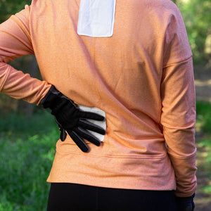 White body warmer by Hothands being applied to the lower back with a gloved hand, another warmer on an orange shirt's upper back.