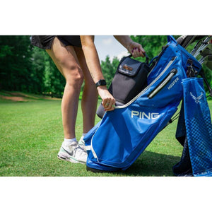 Black soft cooler by Kanga Coolers being placed into a blue golf bag by a woman on a golf course.