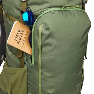 Olive green Asher 65L backpack by Kelty, with a front pocket holding a Field Notes notebook and sunglasses.