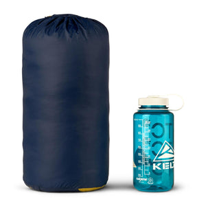Dark blue down sleeping bag by Kelty, compressed in a stuff sack with a yellow base, displayed beside a clear water bottle.