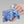 Blue cooling neck wrap by Miracool, inside a clear pouch with a hand pouring water from a bottle into it.