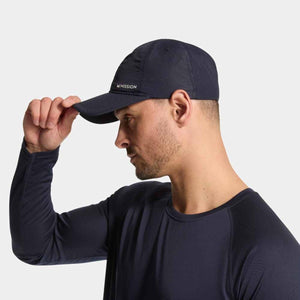 Navy performance hat by Mission with 'MISSION' logo on the brim, being adjusted by a man in a matching long-sleeve shirt.