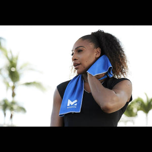 Blue cooling towel by Mission draped around a woman's neck, held to her cheek, featuring the M logo.