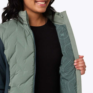 Women's Aria Hybrid Heated Jacket by Mobile Warming with a sage green quilted front, dark teal sleeves, and topographic map lining, worn partially unzipped.