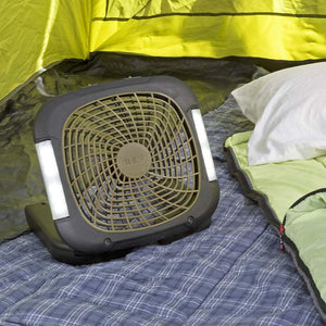 A 10-inch battery camping fan with lights, dark grey and tan, by Treva, placed inside a tent on a plaid blanket next to a sleeping bag.