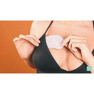 White cooling pads by Opal Cool being placed on a woman's chest over a black bra, with a 58° display.