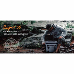 Grey cooler bag by Polar Bear Coolers with a top opening, being accessed by a person outdoors near a rocky river.
