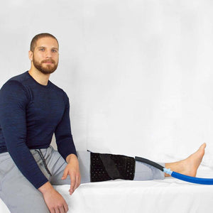 Black cold therapy knee compression pad by Polar Products, worn on a leg with a blue hose, a man sits next to it.