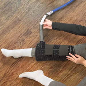 Black full circumference knee compression therapy pad by Polar Products, with Velcro straps and blue hose being adjusted on a leg in white socks.