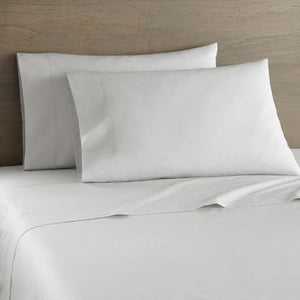 White cotton percale sheet set by Shavel with two matching pillows against a wooden headboard.