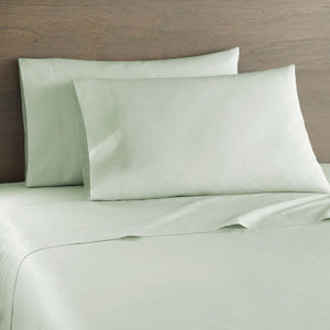 Light green cotton percale twin sheet set by Shavel on a bed with two matching pillowcases and a wooden headboard.