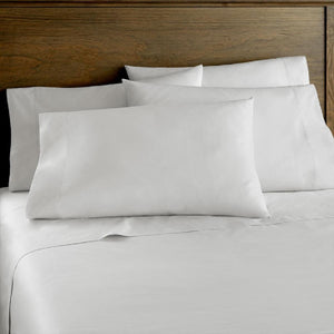 White King cotton sateen sheet set by Shavel, including multiple pillows, on a bed with a wooden headboard.