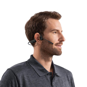 Black bone conduction headset by Shokz with an ear hook and boom microphone, worn by a man in a dark gray polo shirt, side profile.