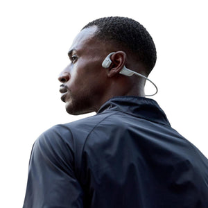Light grey bone conduction headphone by Shokz, worn by a man looking over his shoulder in a dark jacket.