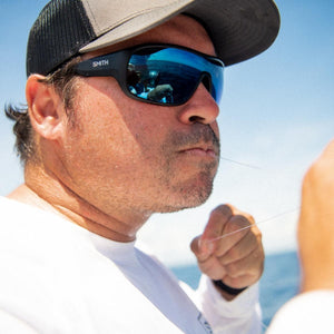 Matte black frame sunglasses with blue mirror lenses by Smith Optics, featuring the 'SMITH' logo, worn by a man fishing.