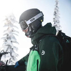 Matte black ski helmet by Smith Optics with yellow MIPS sticker and white striped goggle strap, worn in snow.