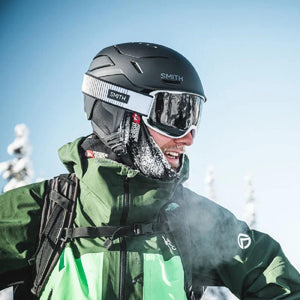 Matte black helmet by Smith Optics, side view, with white-strap goggles on a person wearing a green jacket.