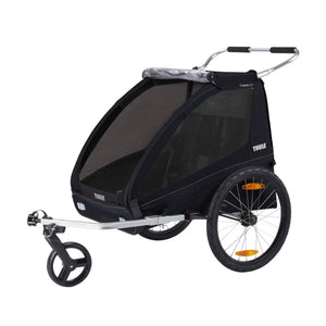Black 2-seat bike trailer by Thule with mesh sides, a front stroller wheel, and large rear wheels, viewed from the side.