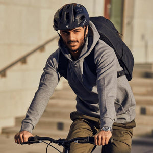 Black backpack from Thule worn by a man riding a bicycle in a grey hoodie.