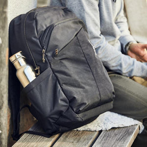 Black fabric backpack by Thule with a silver water bottle in its side pocket, resting on a wooden bench.