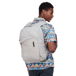 Light grey backpack by Thule worn by a man in a vibrant patterned shirt, with a visible slanted front pocket.