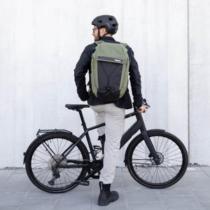 Two-tone green and black backpack by Thule, featuring a bungee system, worn by a cyclist from the back.