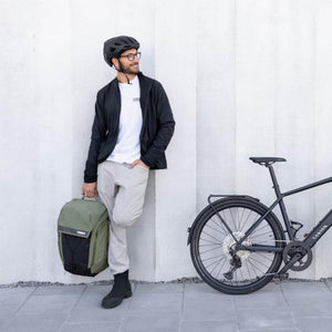 Khaki green and black 28L backpack from Thule, held by a man in a lifestyle shot with a black bicycle.